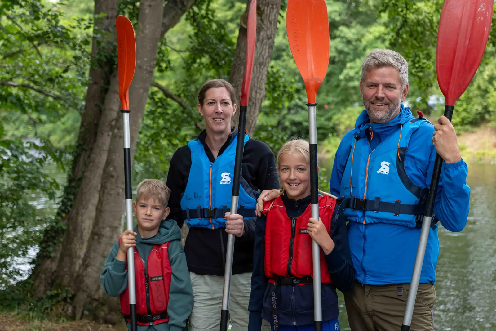Familie in Kanu-Petry-Schwimmwesten mit Paddeln vor dem Start